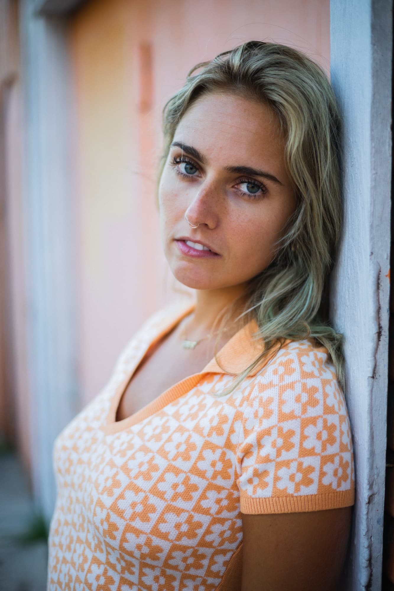 Portrait of a woman in an orange patterned top leaning against a doorway