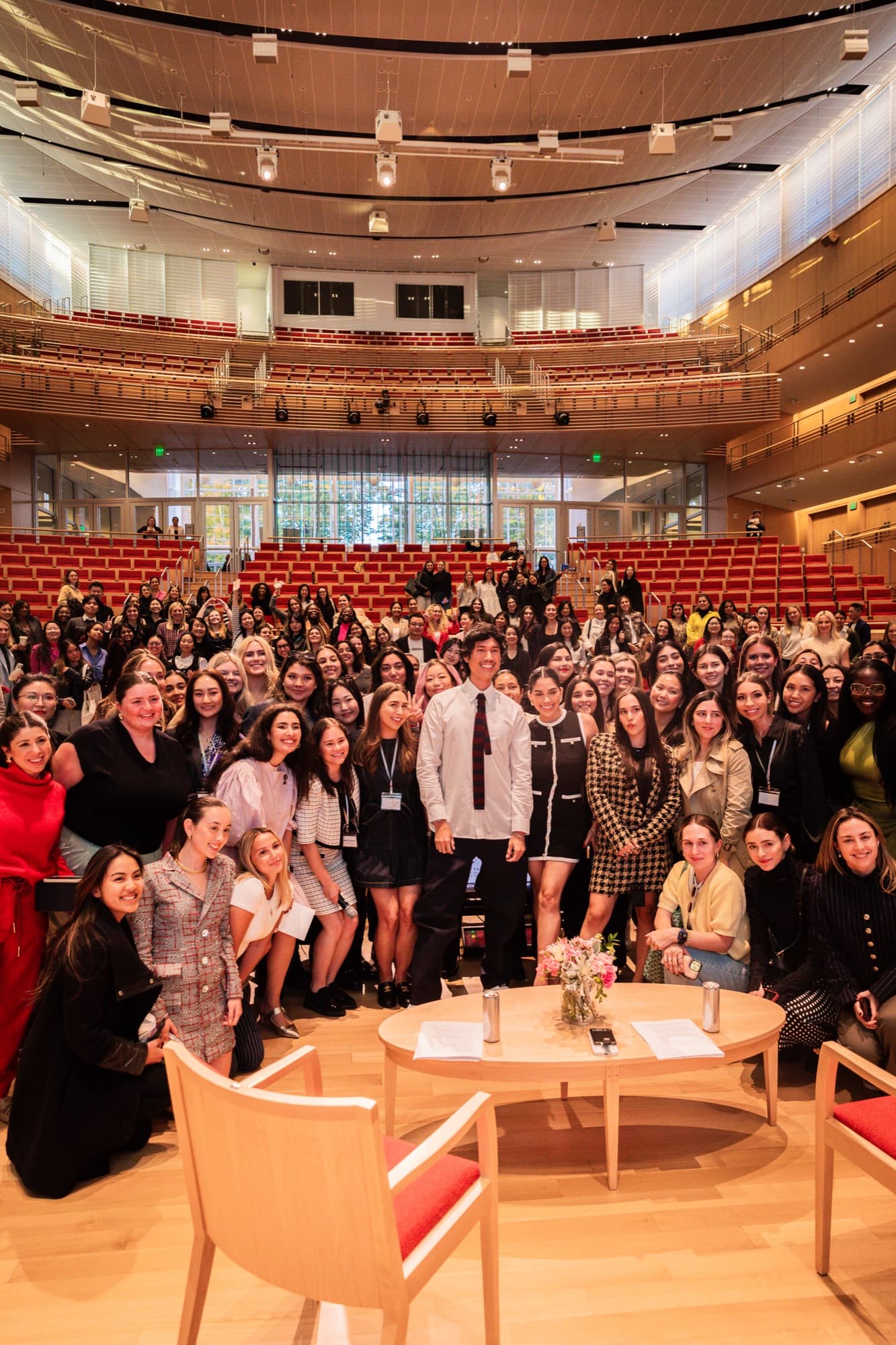 A large audience gathered around two speakers in a Harvard Business School auditorium