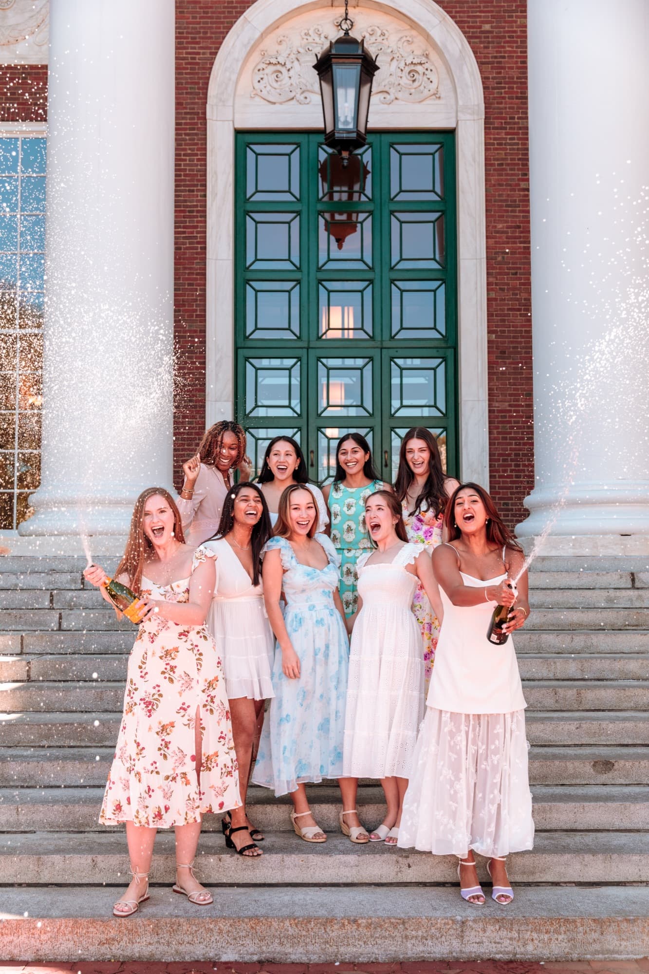 Nine friends celebrating with champagne on the steps of a brick building