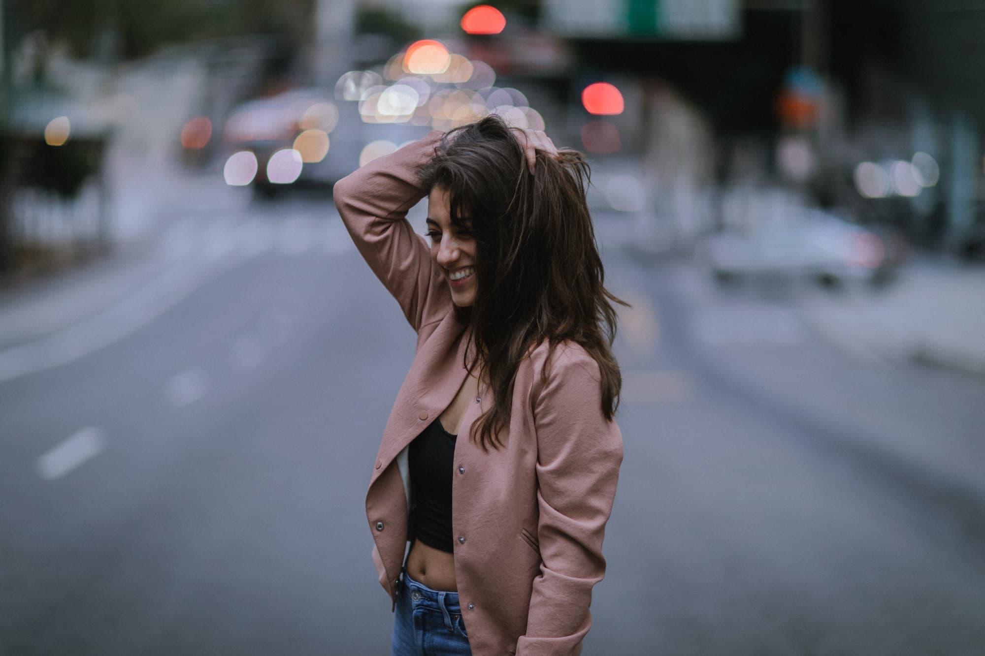 A woman laughing on a city street with evening traffic blurred behind her