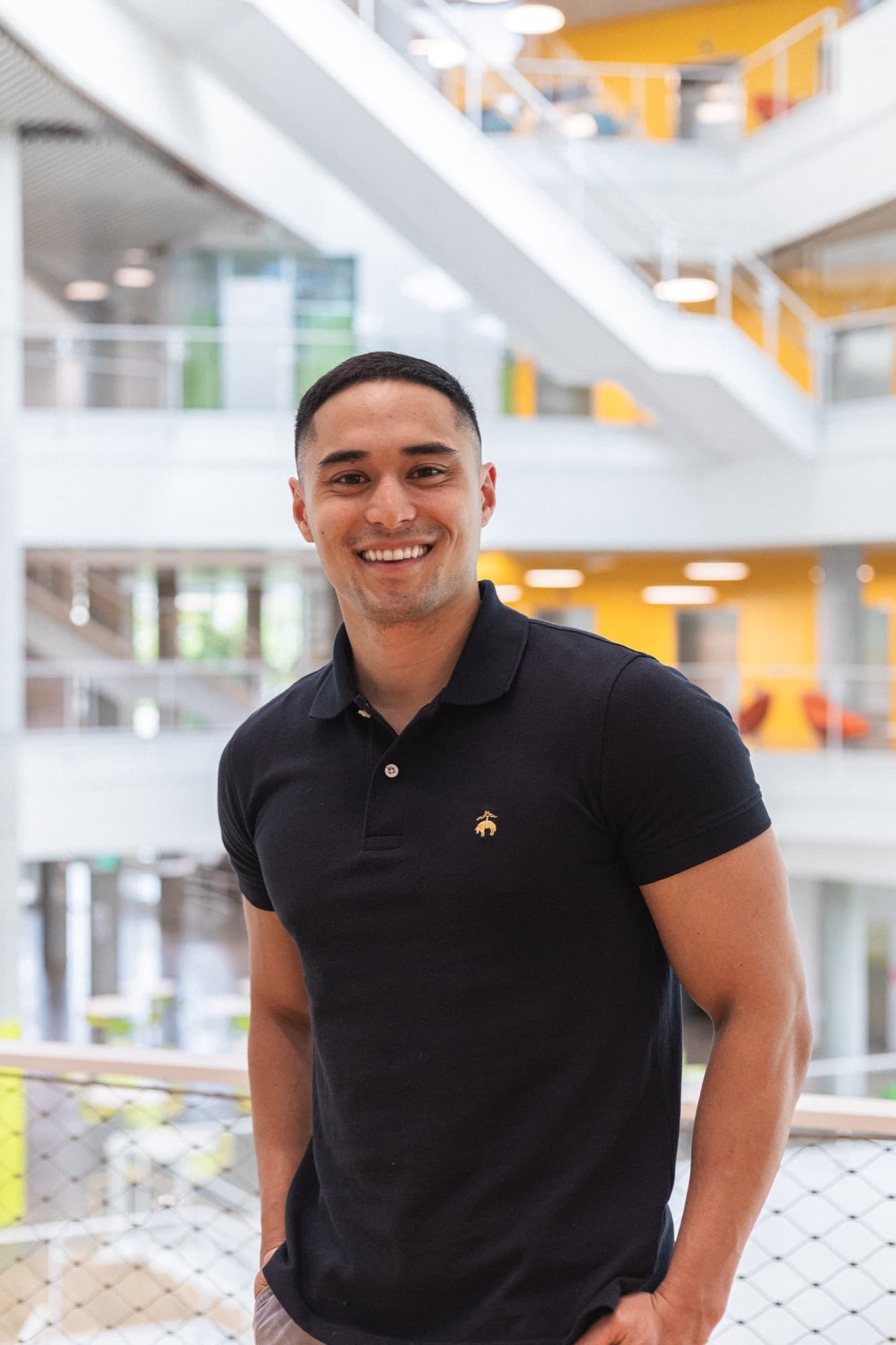 A smiling man in a black polo standing in a bright modern atrium